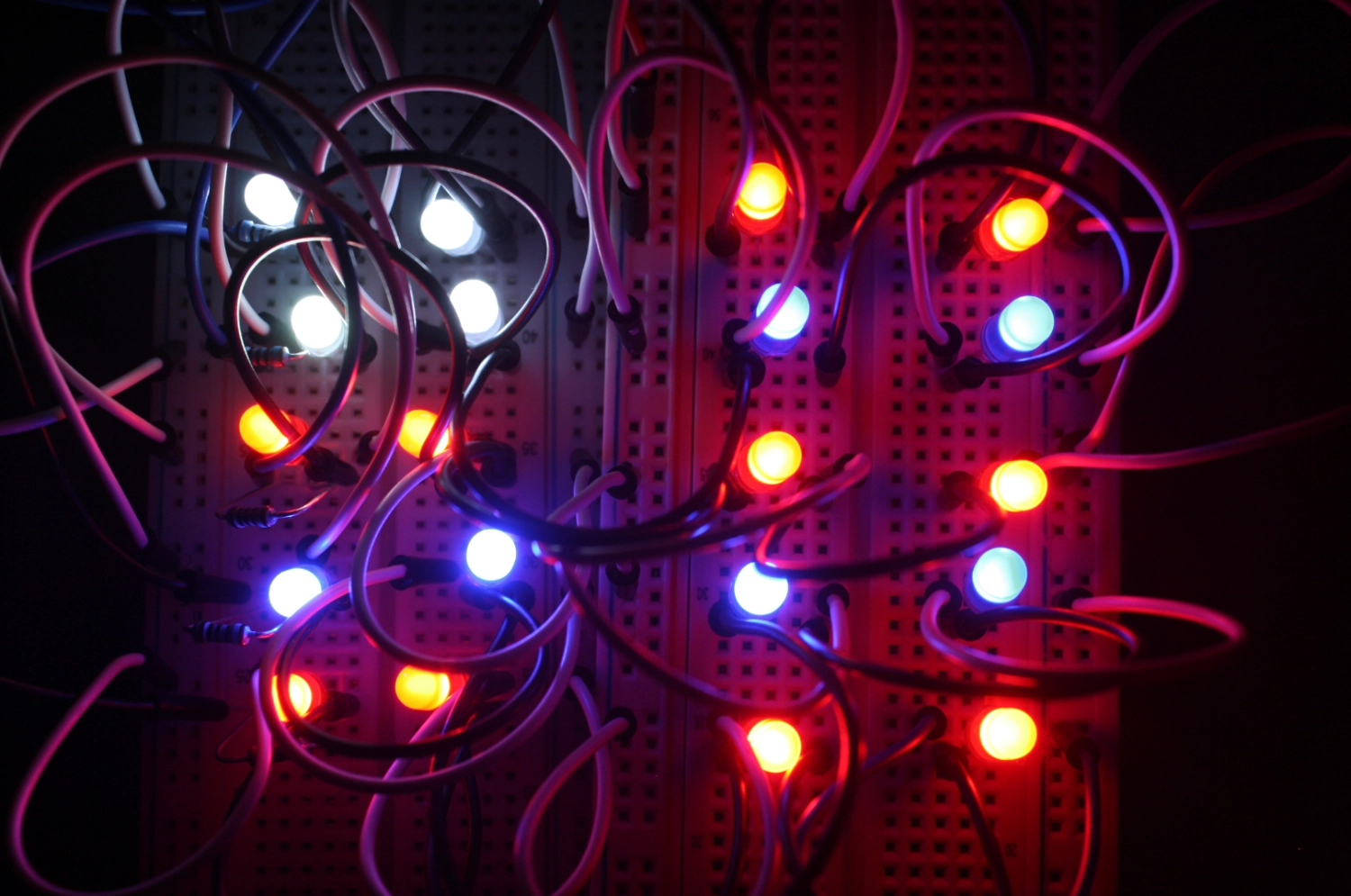 A close-up shot of a breadboard with many colorful LEDs. They are illuminated in red, white, blue, and yellow, connected by a tangled web of wires.